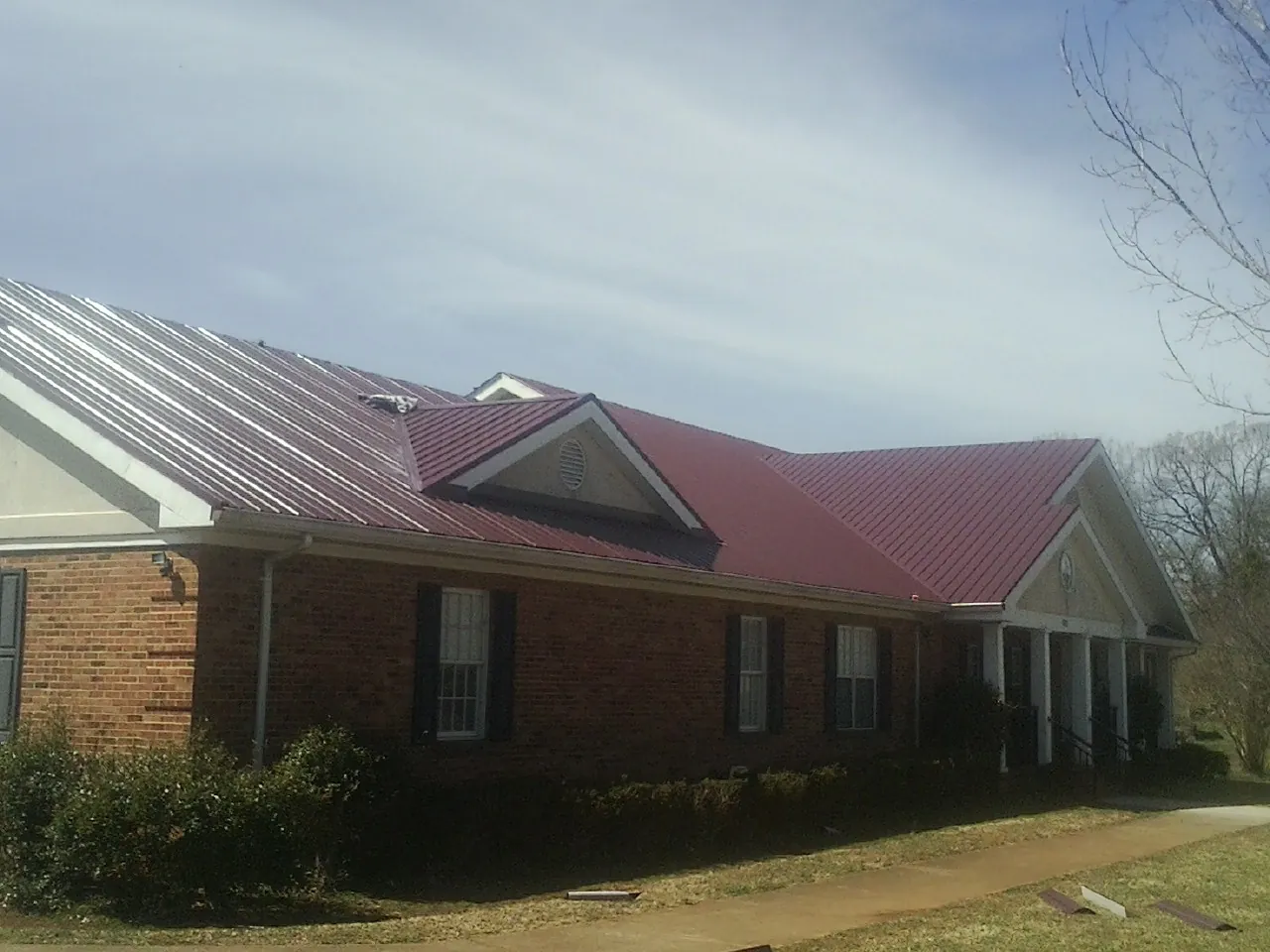 Red metal roof with gabled entries on a long brick building, from a Hail Damage Roof Repair job in Touchet