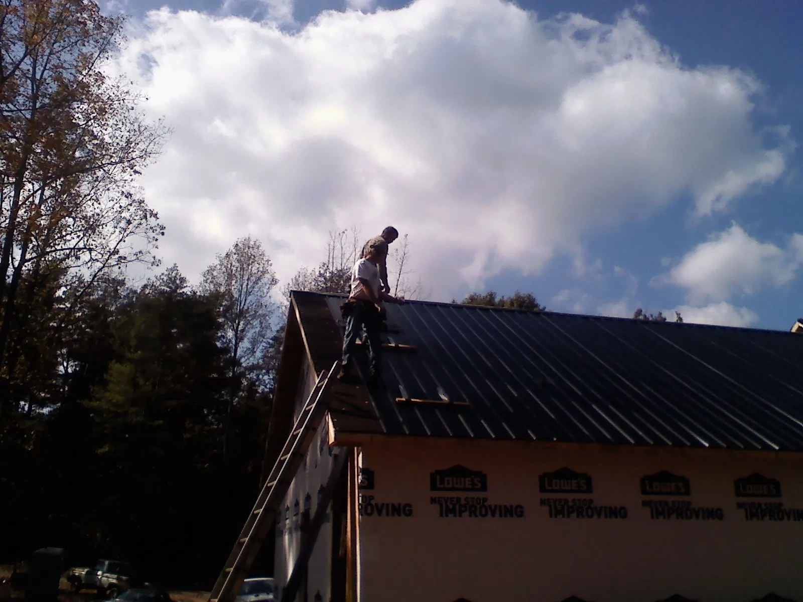 Roofer fastening dark metal panels high against a cloudy sky, from a Roof Inspection job in Touchet