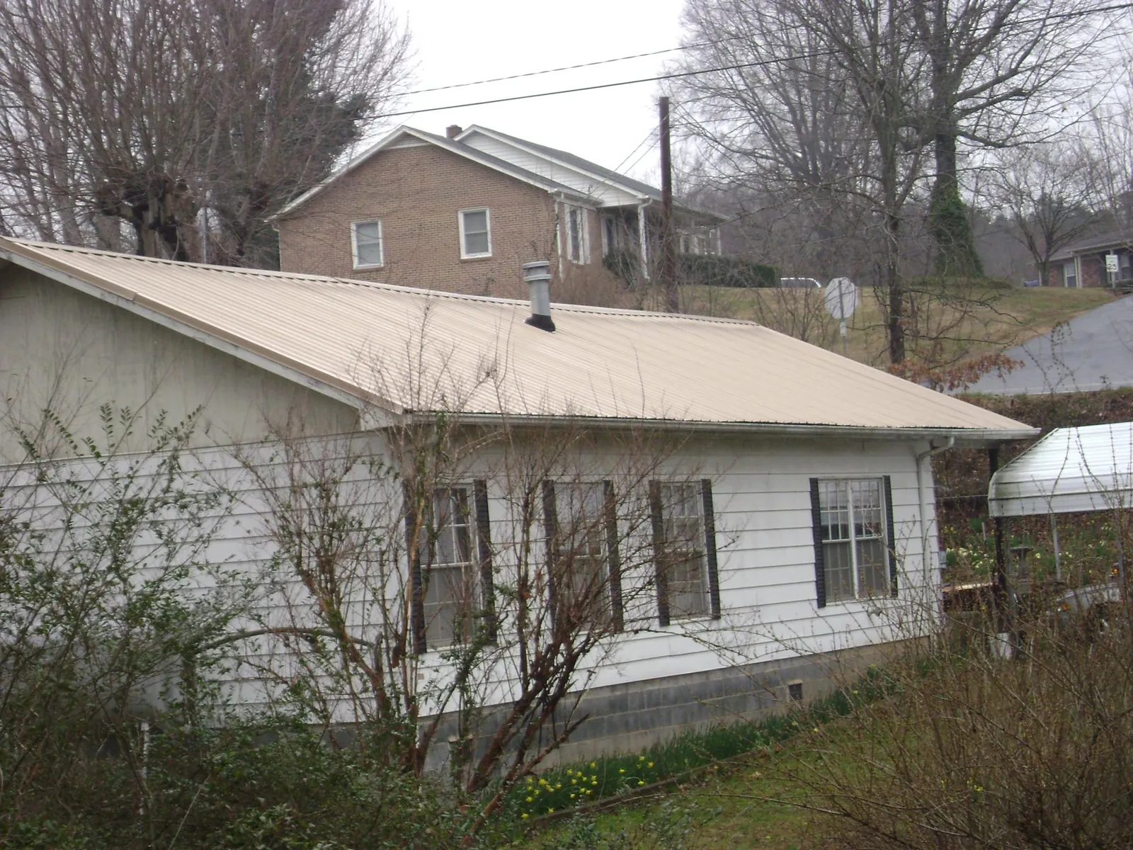 Tan metal roof on a white sided house set into a hillside — Commercial Roofing by Roofing Brothers in Touchet